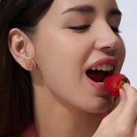 Close-up of a woman eating a strawberry with a focus on her earrings.